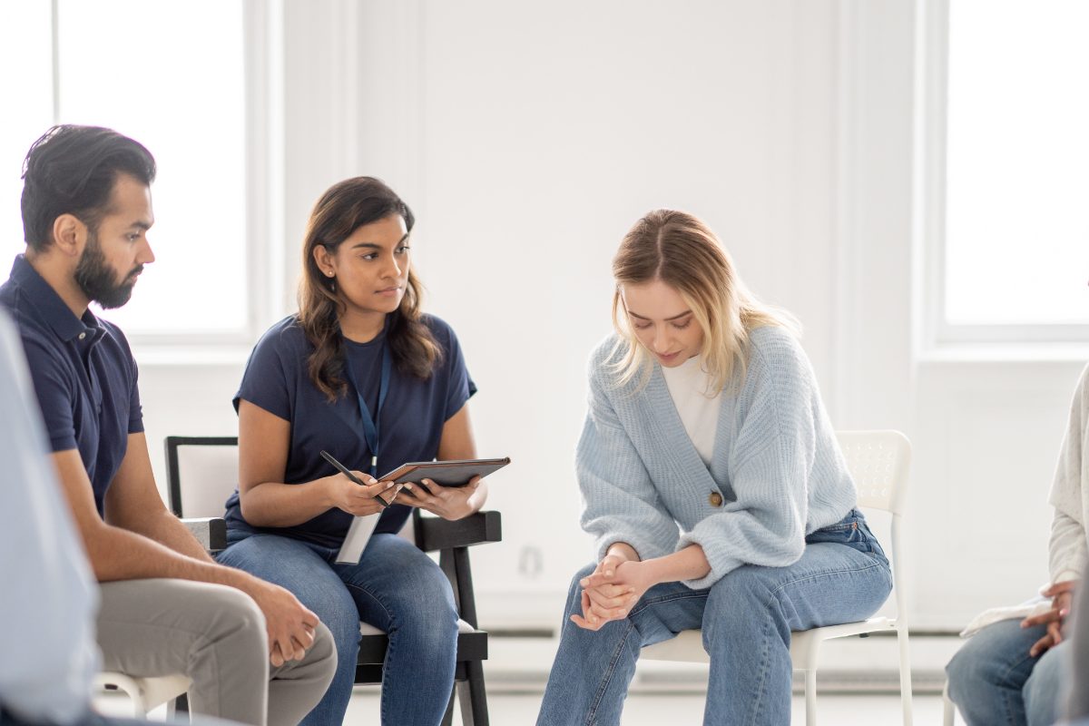 Woman sitting quietly in group therapy, looking down and hesitant to participate, symbolizing resistance to engagement in a counseling session.